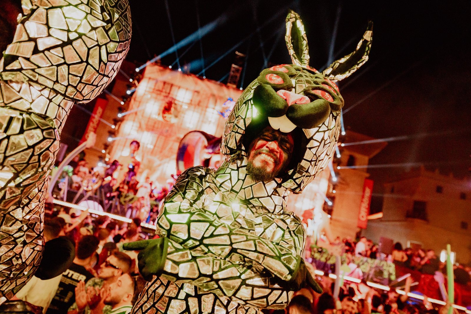 Performer de elrow con un disfraz de serpiente cubierto de espejos frente al público